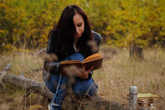 Beautiful woman reading a book in the autumn forest A woman sits near a tree in an autumn forest and holds a book Girl reading a book Autumn season concept and reading