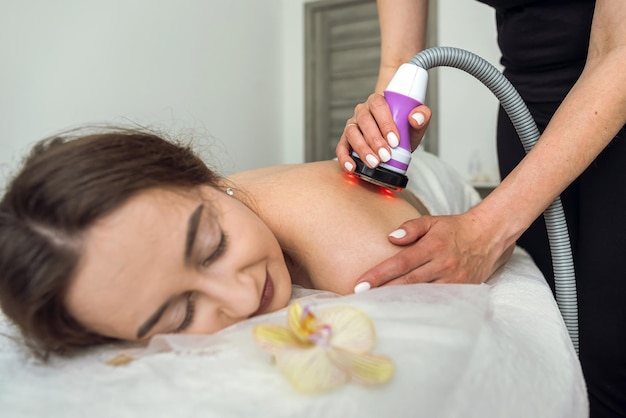 Beautiful woman receives procedure removing cellulite on her back with vacuum massage device