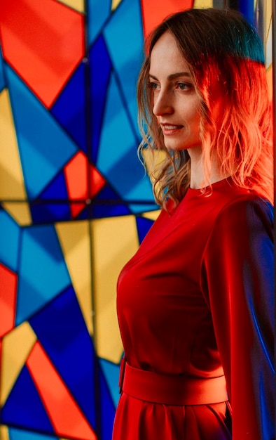 Beautiful woman in red dress in front of colorful stained glass window. European fashion model