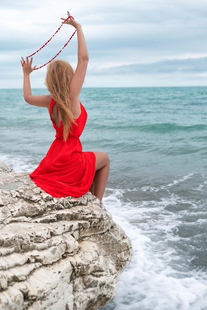 A beautiful woman in a red dress on a white rock by the sea in summer