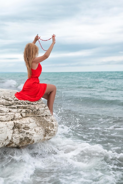 A beautiful woman in a red dress on a white rock by the sea in summer