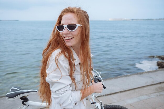 Beautiful woman riding on bike Lifestyle and health in the city Cheerful redhaired young woman gets pleasure from walking around the city