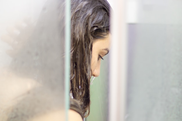 Beautiful woman in the shower behind glass with drops