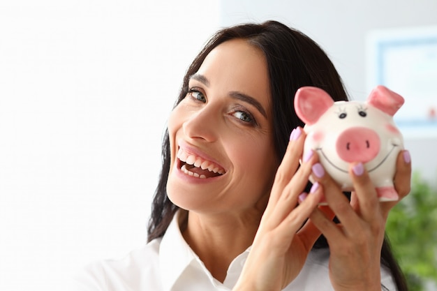 Beautiful woman shows piggy bank and smiles