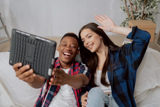 Beautiful woman sits on a couch protected by plastic with her darkskinned fiance a tablet in hands