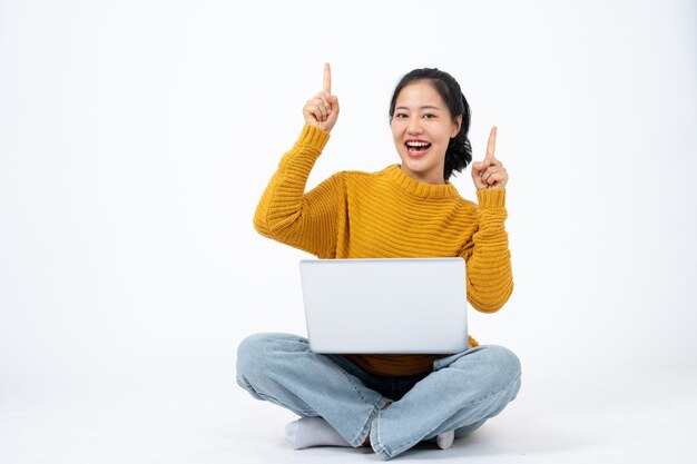 Beautiful woman sits on an isolated white background with her laptop and pointing her finger up