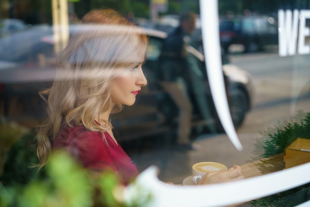 Beautiful woman sitting by the window in a cafe drinking coffee.