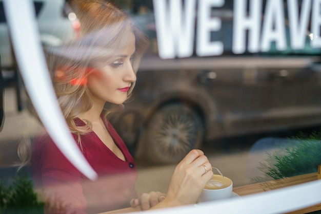 Beautiful woman sitting by the window in a cafe drinking coffee.