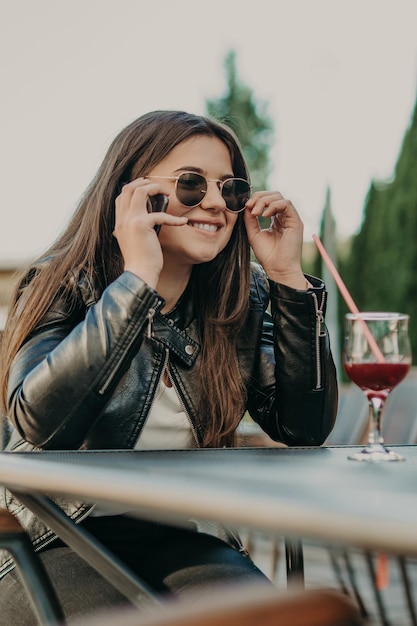 Beautiful woman sitting in a cafe, drinking cocktail and using smartphone. Student during break in the cafe. Lifestyle, technology