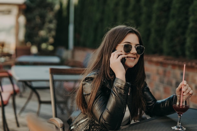 Beautiful woman sitting in a cafe, drinking cocktail and using smartphone. Student during break in the cafe. Lifestyle, technology