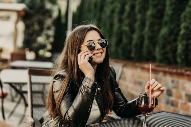 Beautiful woman sitting in a cafe, drinking cocktail and using smartphone. Student during break in the cafe. Lifestyle, technology