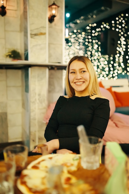 Beautiful woman sitting in chair in pub and smiles woman in black dress is enjoying great evening in...