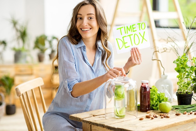 Beautiful woman sitting with healthy green food and drinks at home. Vegan meal and detox concept