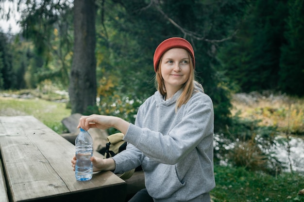 Beautiful woman sitting on a wooden bench with a water bottle in hand A young woman looking over her shoulder and enjoying the beauty of nature