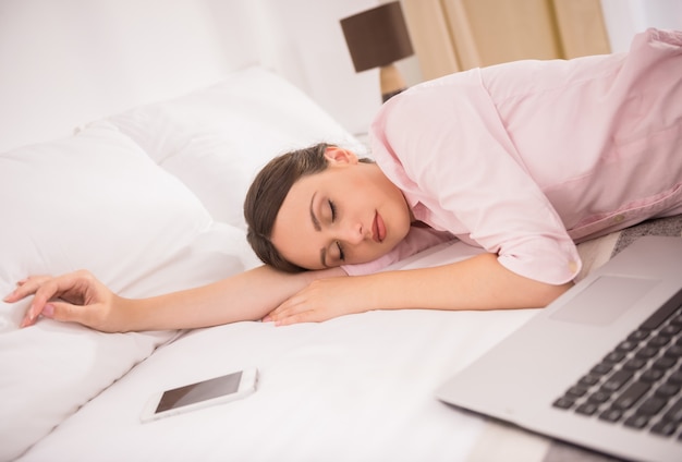 Beautiful woman sleeping on bed with laptop and phone.