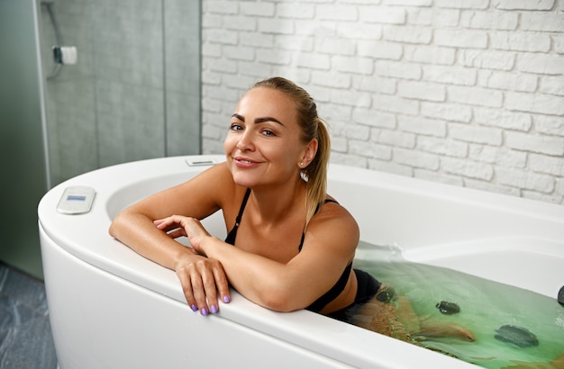 Beautiful woman smiling at camera while enjoying hydromassage and beauty treatments in modern spa capsule at spa center