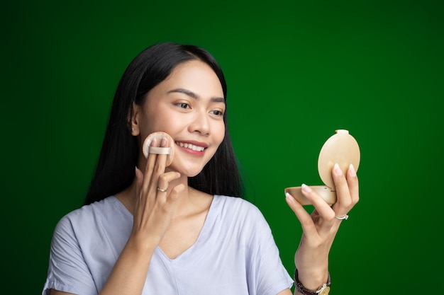 Beautiful woman smiling while using powder puff and holding small mirror while applying make up