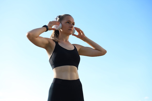 Beautiful woman in sports clothing and earphones looking aside from camera.