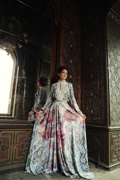 Beautiful woman standing in the palace room with mirror