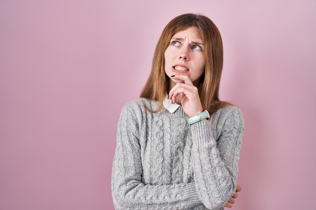 Beautiful woman standing over pink background thinking worried about a question concerned and nervous with hand on chin