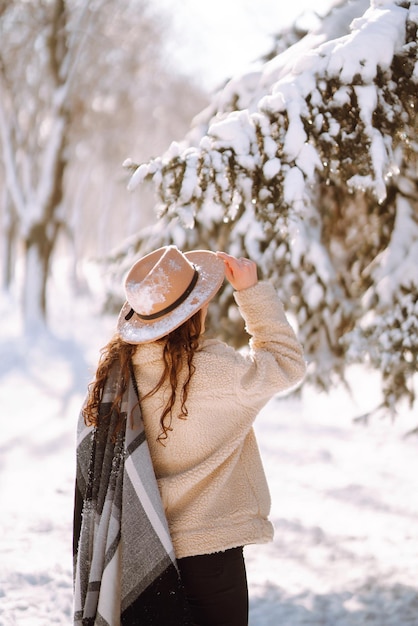 Beautiful woman standing among snowy trees and enjoying first snow. Happy time. Christmas.