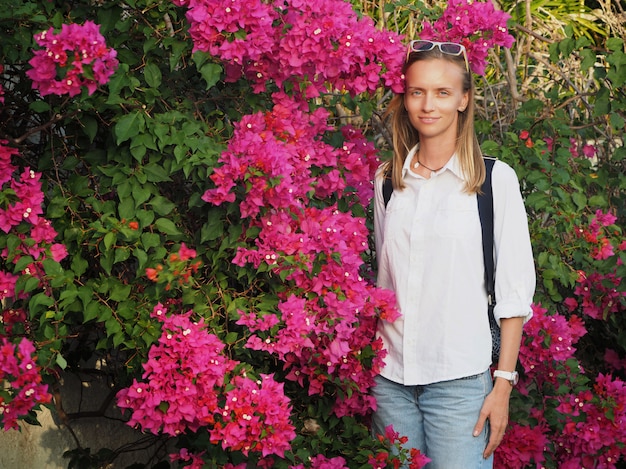 Beautiful woman stands near blooming bushes of flowers