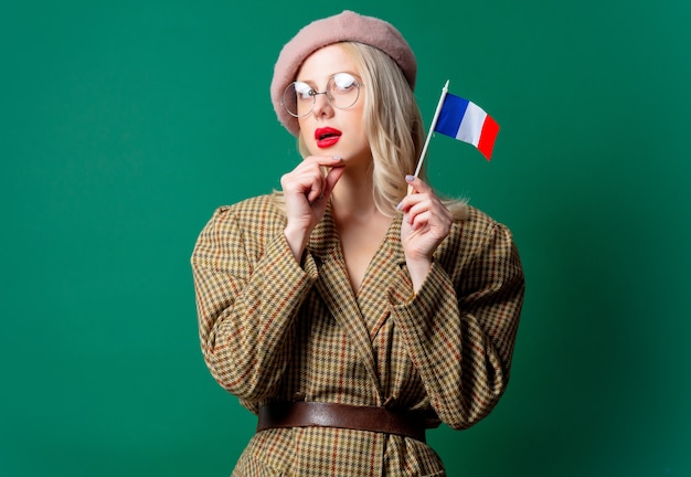 Beautiful woman in style jacket and hat with French flag on green wall