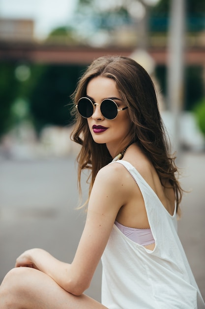 Beautiful woman in sunglasses sitting on the asphalt