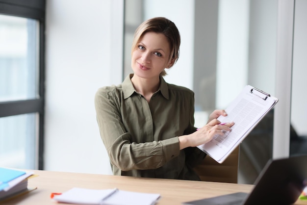 A beautiful woman at a table in the office shows documents a closeup financial presentation