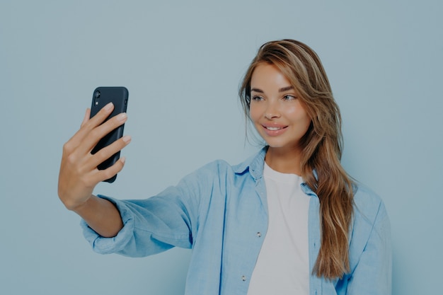 Beautiful woman taking photo of herself on light blue background