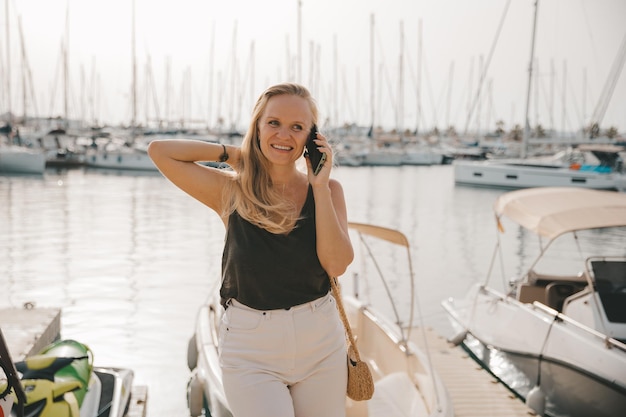 Beautiful woman in talking on the phone against the backdrop of the blue sea and yachts