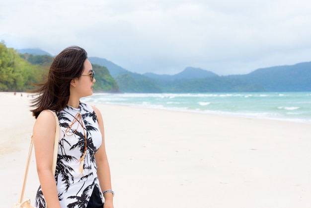 Beautiful woman tourist wearing sunglasse smiling looking at the nature landscape of the beach and the sea in summer sky on Tarutao island National Park, Satun, Thailand