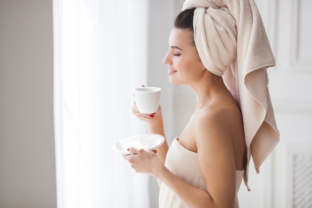 Beautiful woman in the towel after bathing drinking morning coffee