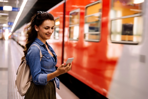 Beautiful woman using her cell phone on subway platform. Transportation Concept.