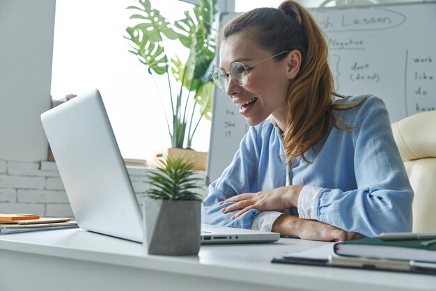 Photo beautiful woman using laptop while sitting near the whiteboard at classroom