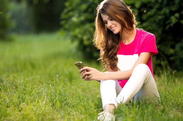 Beautiful woman using phone while sitting on grass in the green park