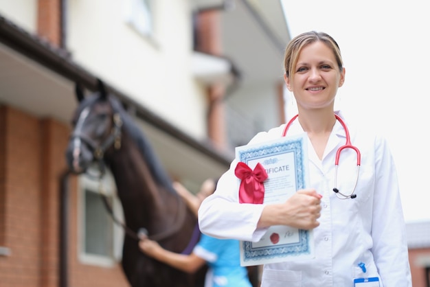 Beautiful woman veterinarian is holding medical certificate next to horse