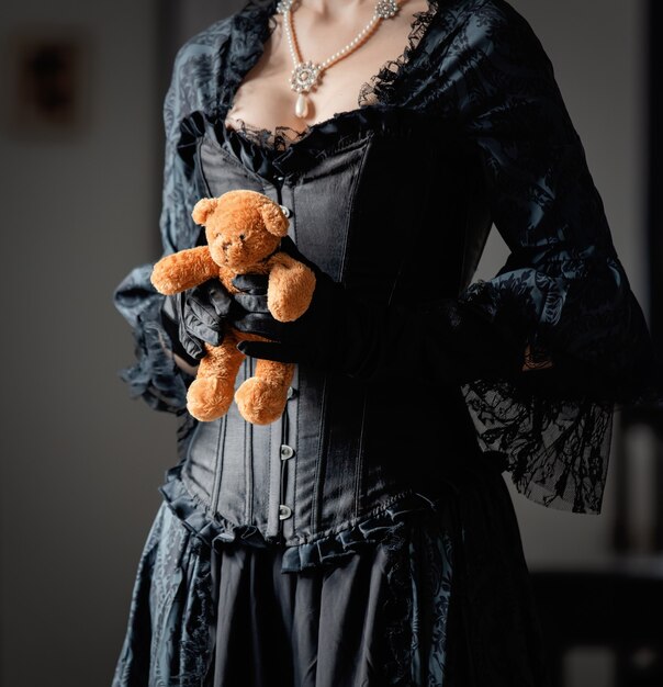 Beautiful woman in vintage black dress holding a teddy bear toy