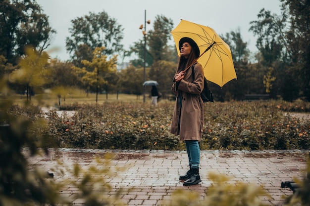 Beautiful woman walking in the park while holding a yellow umbrella during rainy day