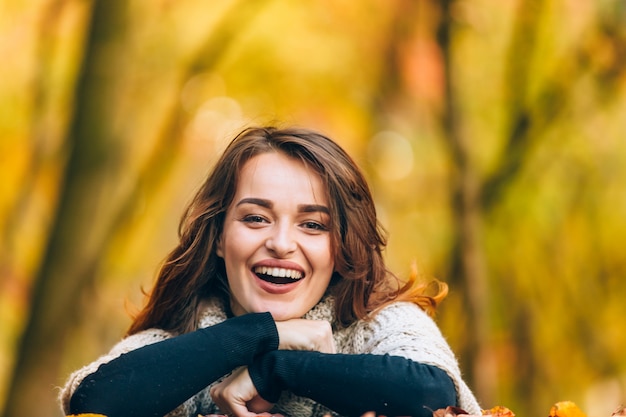 Beautiful woman in warm clothes laughs in the park on the of trees in the autumn.