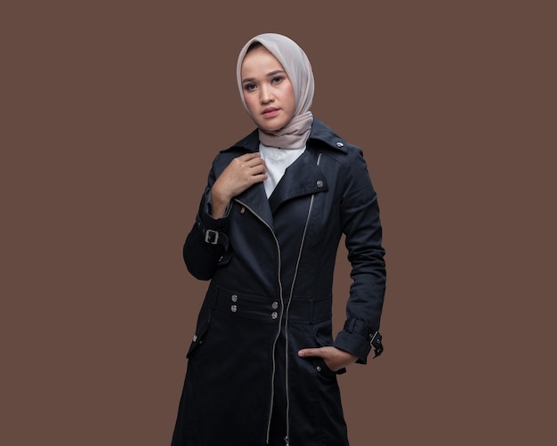 Beautiful woman wearing hijab posing while putting her hands into her coat pocket isolated on plain background