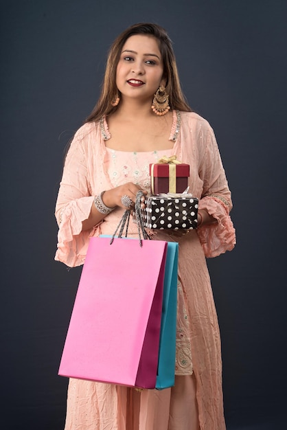 Beautiful woman wearing Indian traditional dress holding shopping bags and gift Box on a grey background