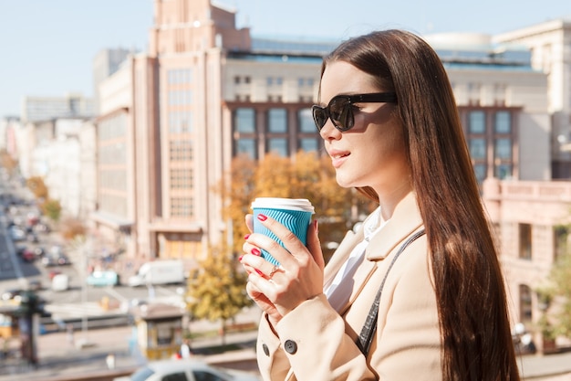 Beautiful woman wearing sunglasses, drinking coffee in city center