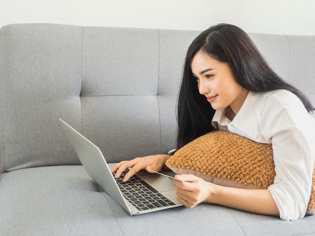 Beautiful woman in a white dress, playing a laptop computer on the sofa. Business ideas and online shopping