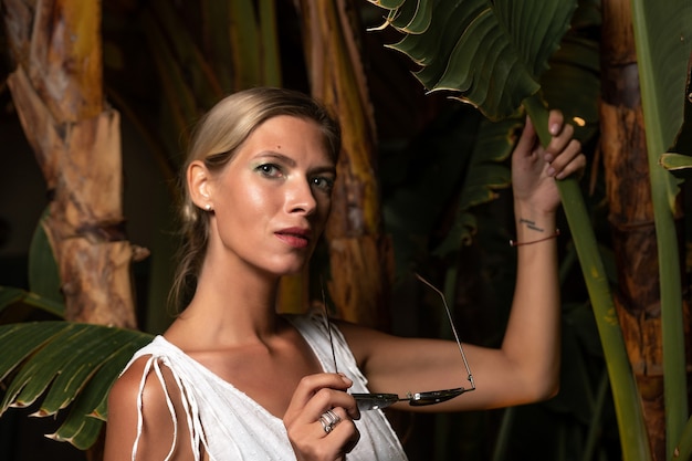 Beautiful woman in a white dress posing on the leaves backdrop.