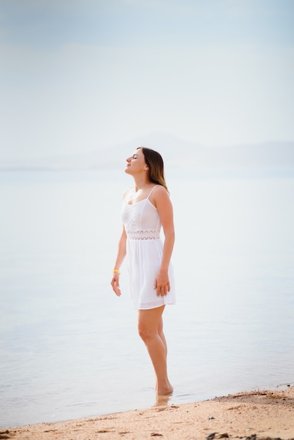 Beautiful woman in a white dress walking on the beach