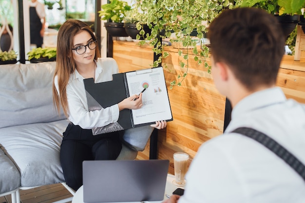 beautiful woman in a white shirt shows charts for her boss, on the summer terrace of the modern office.