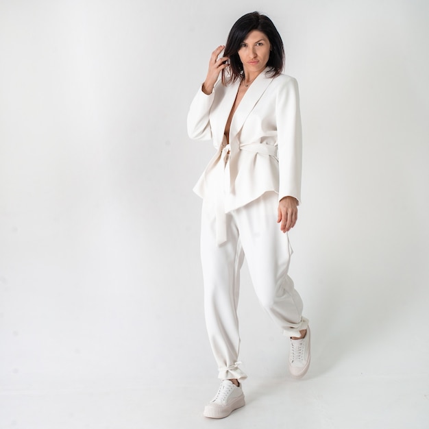 Beautiful woman in a white trouser stylish suit and white shoes on a white background