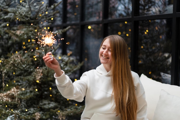 Beautiful woman in winter suit walks among the fir trees and lights sparklers