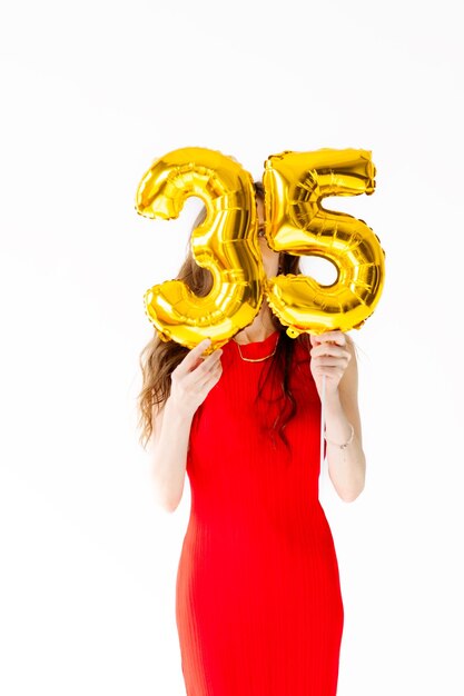 Beautiful woman with balloons and the numbers 35 is photographed in the studio in a red dress